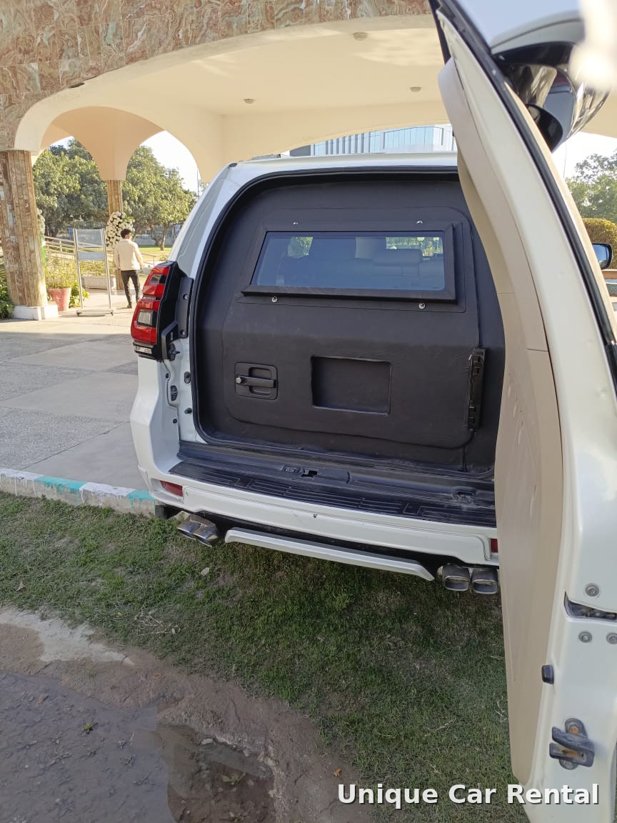 White armored Toyota Prado with rear door open showing the ballistic compartment